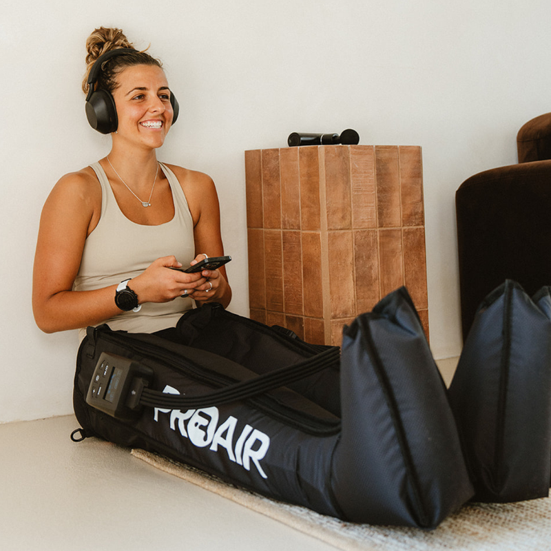 Woman seated with her phone wearing PROAir wireless compression boots