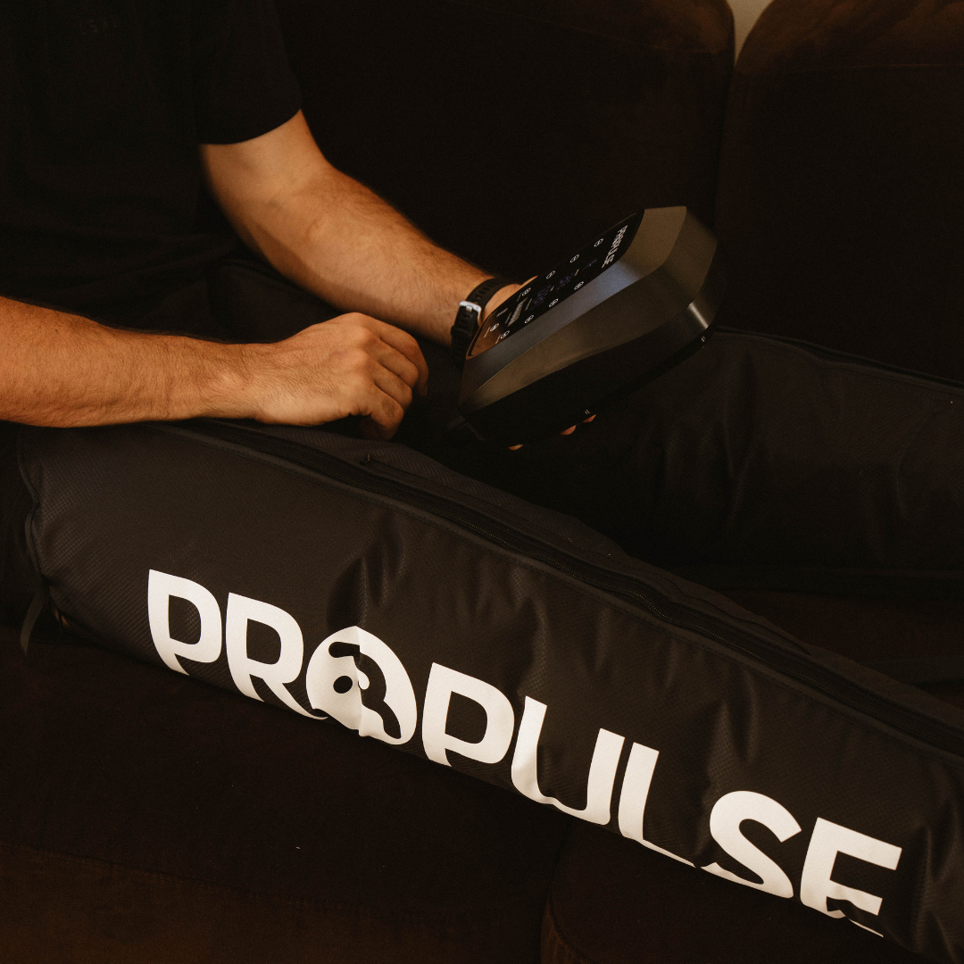 Man on a couch holding the PROPulse control unit while wearing PROPulse compression boots