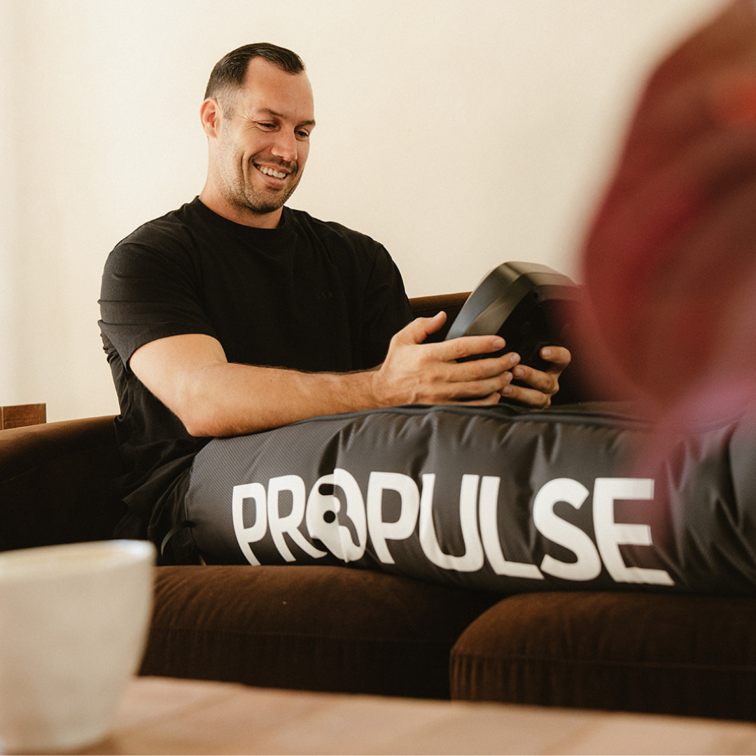 Man on a couch holding the PROPulse control unit while wearing the leg attachments